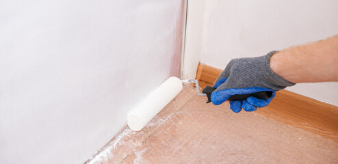 A man paints a wooden door white. The painter uses a foam paint roller to apply white acrylic paint on the door.