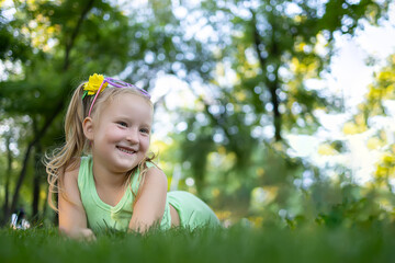 a little cheerful girl in a green suit lies on the grass in the park and looks away