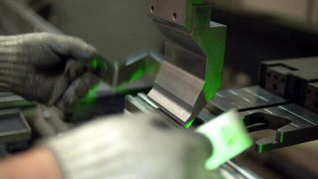 The employee hands are not bending the large parts of the metal on the bending machine, closeup. The CNC operator bending a metal product bends. The employee works at the metal factory.