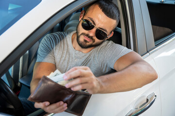 The young man pays for fuel in cash. A handsome man counts money near the car. Fuel and oil crisis....
