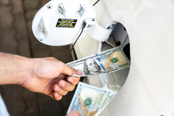 Hand of the man putting money into the opening gas tank of his car.  Refueling car with gasoline at...