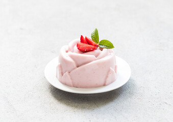 Vegan Strawberry cream pudding, Panna Cotta, in the shape of a rose, on a plate. Light grey background