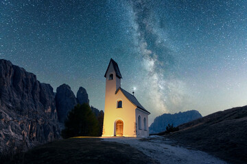 Incredible view on small iIlluminated chapel - Kapelle Ciapela on Gardena Pass, Italian Dolomites mountains. Glowing Milky Way in starry sky on background. Dolomite Alps, Italy. Landscape photography - Powered by Adobe