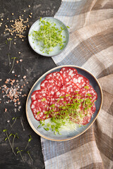 Slices of smoked cervelat salami sausage with spinach microgreen on black, top view, close up.