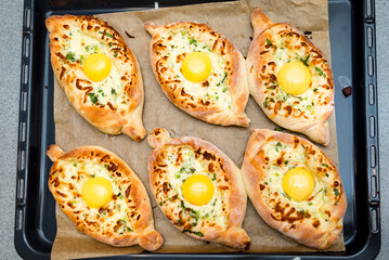 Adjarian khachapuri in the shape of a boat. Six portions on a baking tray as seen from above. A fluffy serving of hot khachapuri with a fatty egg yolk and two kinds of cheese.
