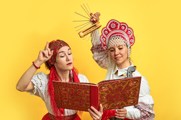 Women musicians in Russian folk dresses with musical instruments on a yellow studio background....