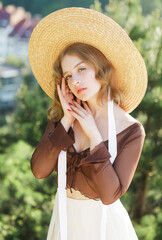 Portrait of a beautiful young girl in a straw hat, posing against the background of the city from...