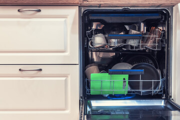 Obraz premium The dishwasher is filled with clean dishes after washing. Dishwasher with open door and washed plates and cups inside