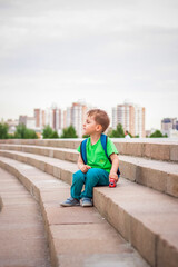 A boy is playing with a toy, sitting on the steps in the open air against the backdrop of skyscrapers and high-rise buildings. Journey. Lifestyle in the city.