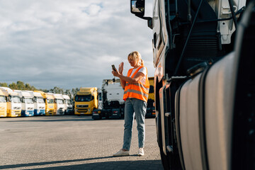 Caucasian middle-aged woman having a phone call in front of yellow semi-truck vehicle 