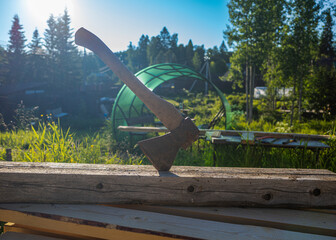 an old axe stuck in a log, the background of a construction site in the forest and the rays of the sun