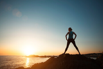 A female yogi does gymnastics on the oceanfront during a beautiful sunset.