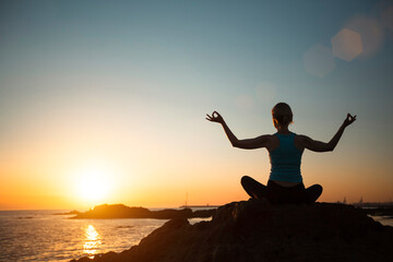 Yoga woman on ocean coast meditation during beautiful sunset.