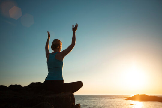 A yoga woman, raising her hands to the sky on the sea beach during a beautiful sunset.