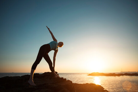 Fitness lady doing gymnastics by the Sea beach during a beautiful sunset.