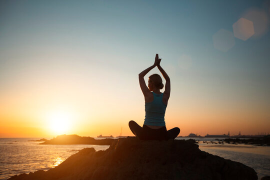 Yoga woman in Lotus position on ocean coast relaxation during beautiful sunset.