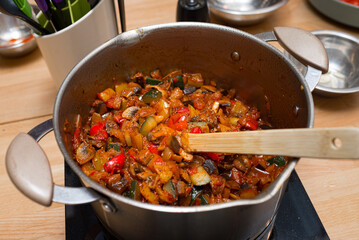 sautéed vegetables in a pot on an electric stove with a wooden spatula. top view of the kitchen table.