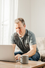 A young man studies and works at home with a laptop. Freelancer checks mail, writes letters and uses internet banking services