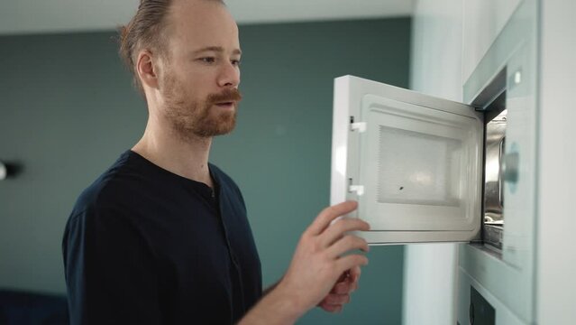 Concentrated blond man heats food in the microwave at home