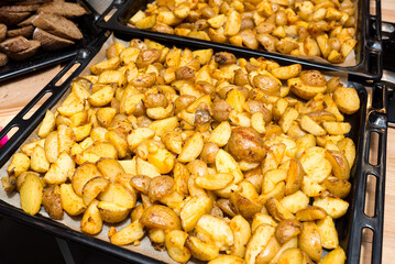 Slices of baked potatoes with skin and crispy crust on a baking tray from the oven.
