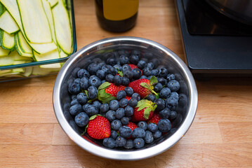 A deep metal bowl of berries on the kitchen table. Fresh blueberries and strawberries.