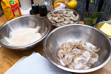 Raw seafood in a metal bowl. Cooking preparations. Bowl with uncooked shrimp. Bowl with raw squid. Table with billets.