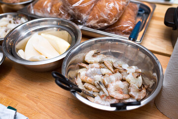 Raw seafood in a metal bowl. Cooking preparations. Bowl with uncooked shrimp. Bowl with raw squid. Table with billets.