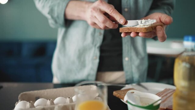 Man wearing shirt spreading cottage cheese on the bread in the kitchen at home