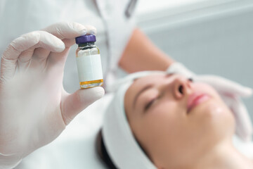 A woman holds a cosmetic product in her hand. Solution for injection.