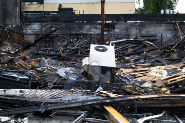 Building burned to the ground. Complete destruction of building after fire started in the basement. Charred collapsed structure with wood beams, bent metal railing and ac unit. Selective focus. - obrazy, fototapety, plakaty