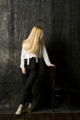 Fototapeta na wymiar portrait of a beautiful blonde woman with long hair in a white blouse and black trousers on a gray isolated background.a charming girl posing on a dark background.