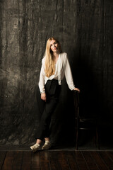 Obraz na płótnie Canvas portrait of a beautiful blonde woman with long hair in a white blouse and black trousers on a gray isolated background.a charming girl posing on a dark background.