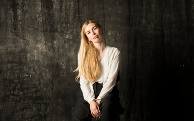 Fototapeta premium portrait of a beautiful blonde woman with long hair in a white blouse and black trousers on a gray isolated background.a charming girl posing on a dark background.