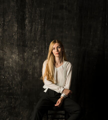 portrait of a beautiful blonde woman with long hair in a white blouse and black trousers on a gray isolated background.a charming girl posing on a dark background.
