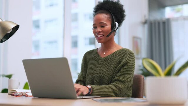 Confident black female call centre agent talking on a headset while working on a laptop in an office. Confident African American consultant operating a helpdesk for customer service and support