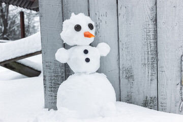 One snowman with button eyes and a carrot nose stands in a snowdrift on a gray wooden background