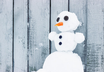 One snowman with button eyes and a carrot nose stands in a snowdrift on a gray wooden background