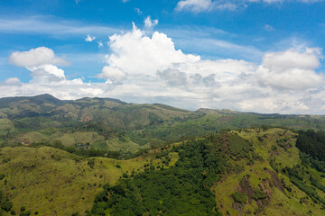 Fototapeta premium Green hills with tea estates in a mountainous area against a background of blue sky and clouds. Sri Lanka.