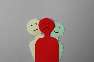 Colorful paper cutouts of person with different emotions on grey background, top view