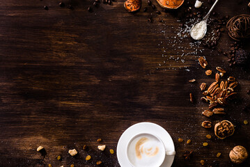Flat lay wooden background dark brown wood. A cappuccino cup, sprinkled sugar, walnuts, raisin and...