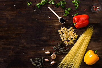 Various sorts of pasta on top of a dark wooden background. Farfalle, fusilli, spaghetti, bell...