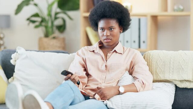 Trendy woman watching a boring movie, decides to use phone instead. Young girl addicted to social media, looks bored while trying to watch TV but switching between channels with a remote control