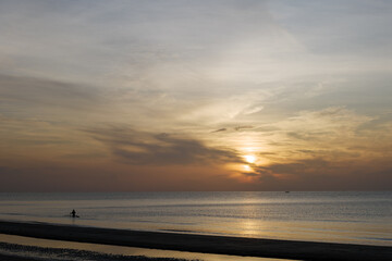 Outdoor sunny silhouette view of a sea, sky, beach and fisherman trawl on water during sunset or sunrise time.