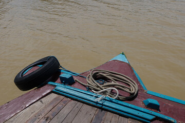 Fototapeta premium Low angle sunny view at the bow, front of the boat, with wooden floor float straight ahead along river with background of riverside of the countryside of Ayutthaya province in Thailand. 