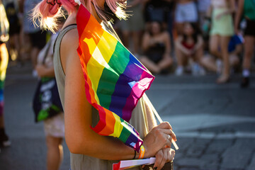 Young woman, pink-haired girl holding a rainbow LGBT flag in hand on Pride Month. Lesbian, gay, bisexual people at parade, festival have fun joy. Crowd of people at a celebration. Tolerant community.