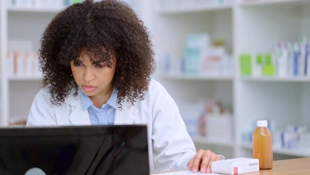 Young and busy pharmacist checking her computer while stock taking and dispensing medicine in a pharmacy drugstore. Female health professional or chemist filling out prescription medication documents
