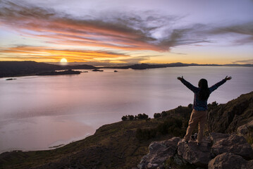Tourist with arms up enjoying the sunset over Lake Titicaca from the island of Amantani, Puno - Peru.