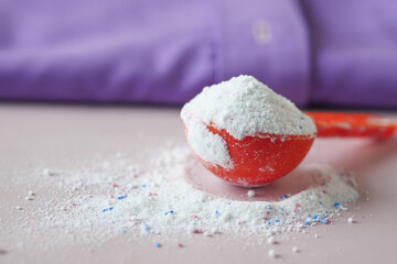 Washing powder in plastic spoon on blue background 
