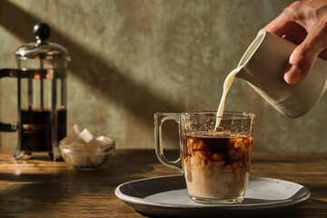 pouring milk into the coffee with a jug with coffee pot and sugar cubes in the background...