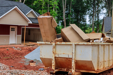 On the underside a house there is an industrial dumpster full of rubbish removal containers